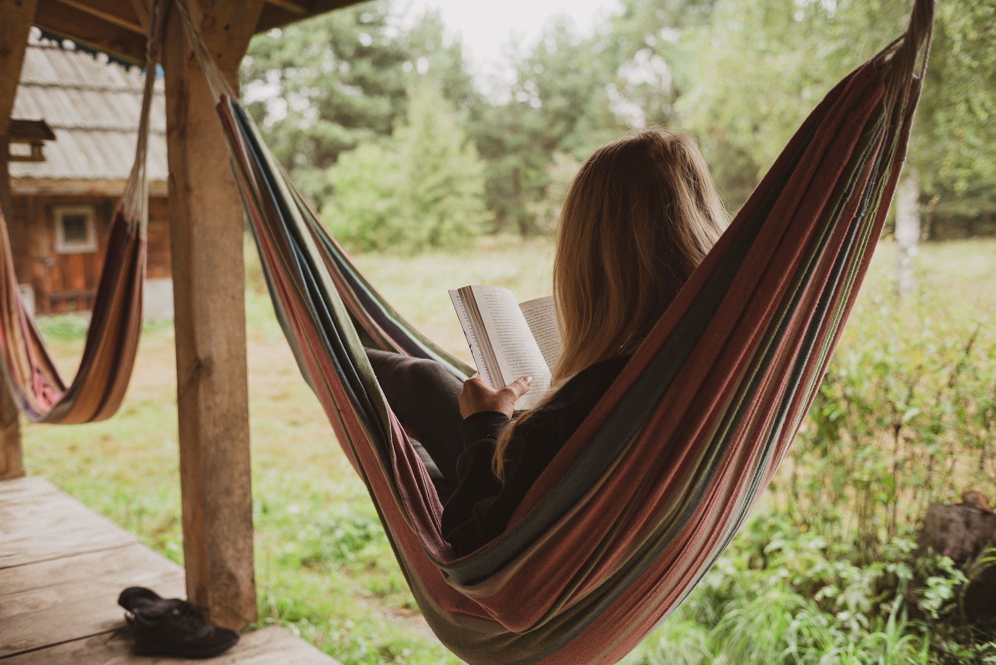 Person liegt in der Hängematte im Garten und liest ein Buch